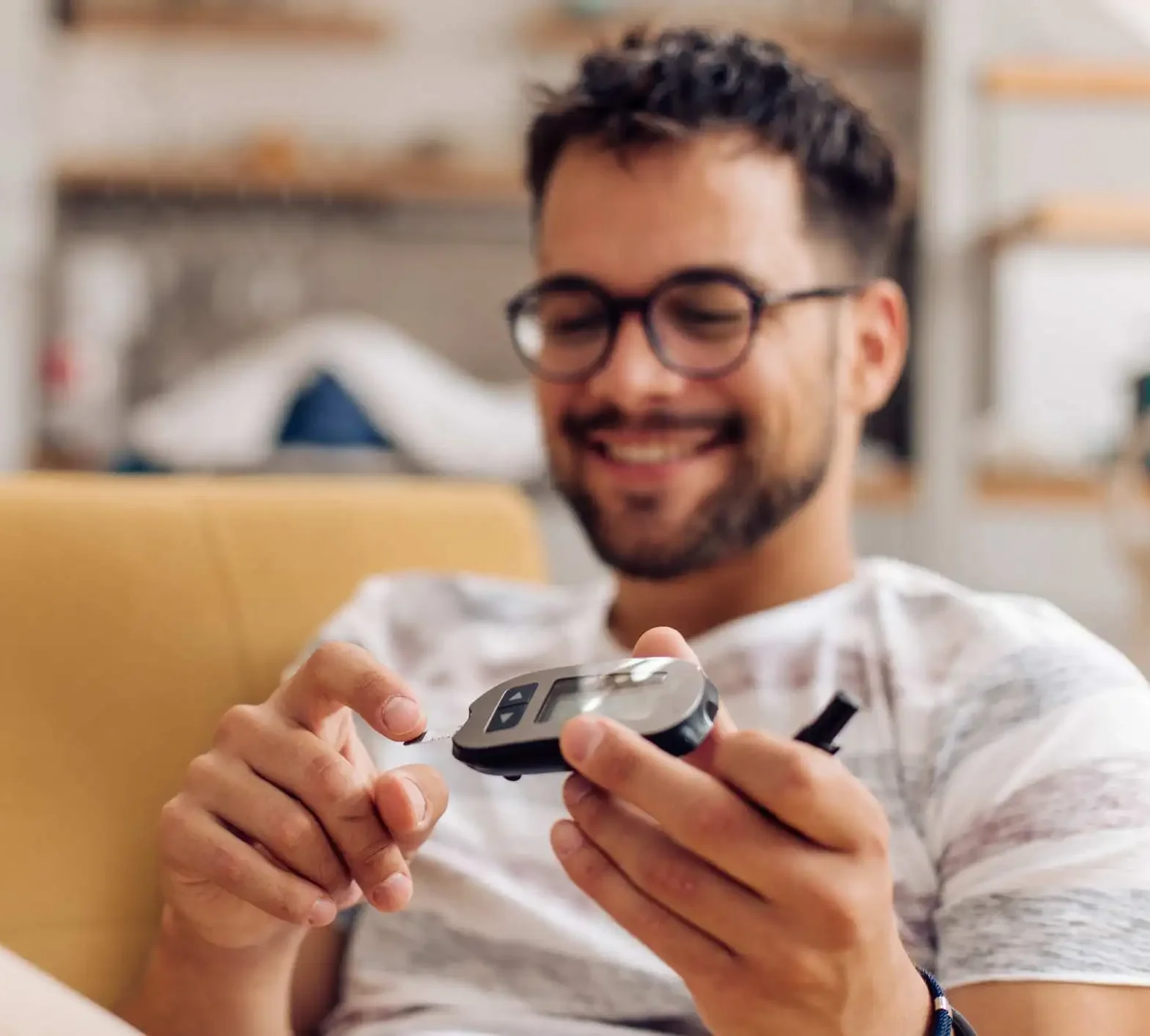 Smiling man checking blood sugar levels on a sofa