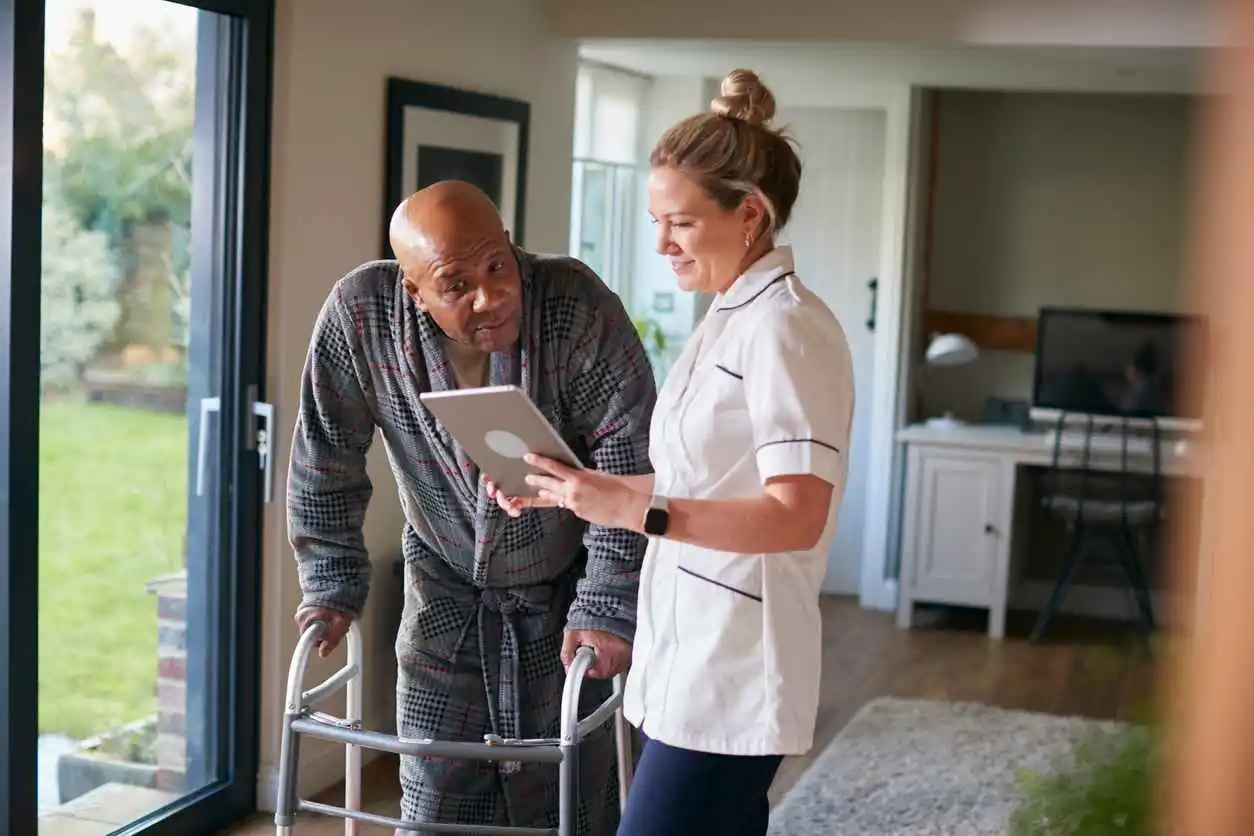 Nurse showing a man using a zimmer an ipad in his home