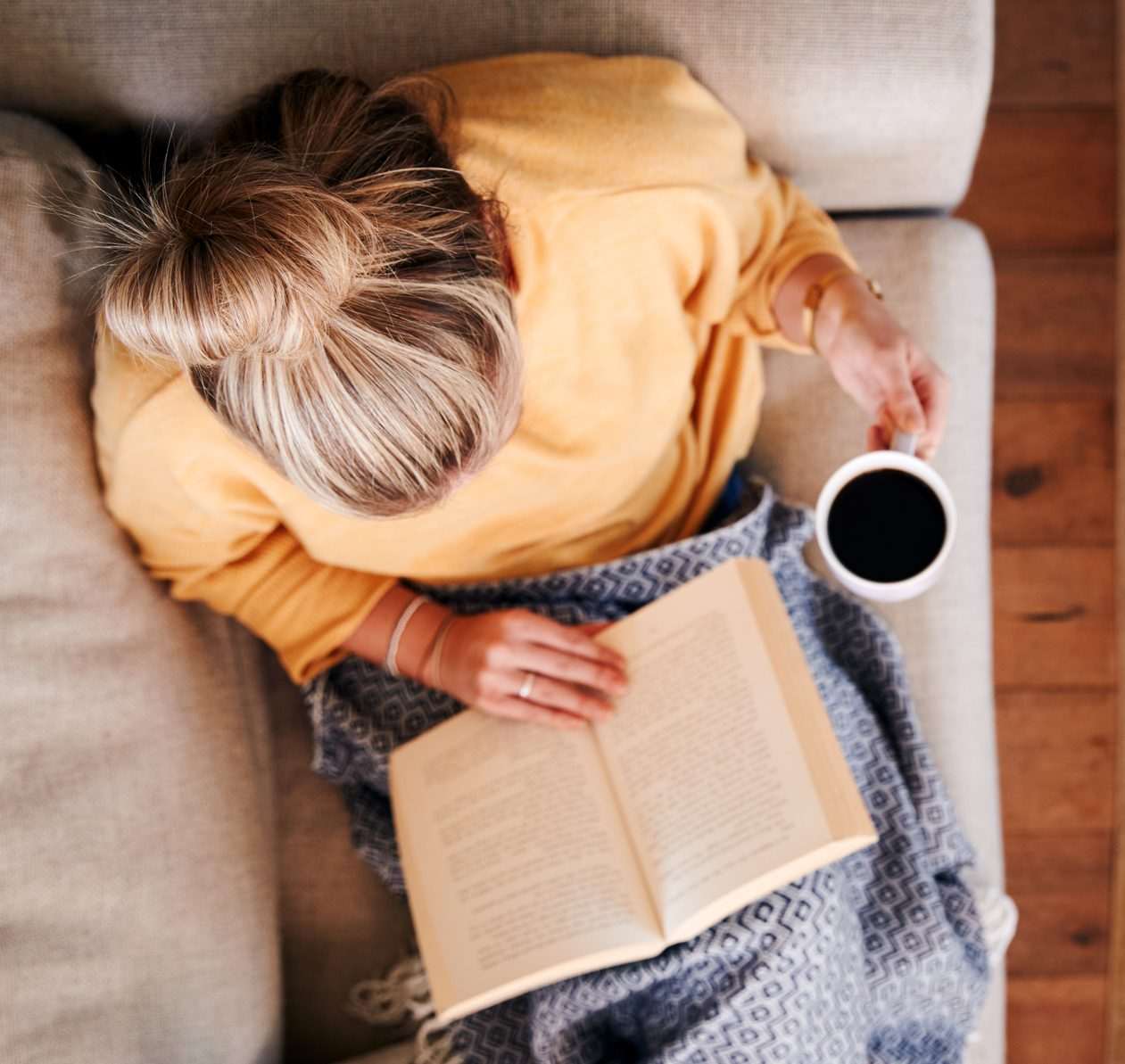 woman reading a book on the sofa with a hot drink