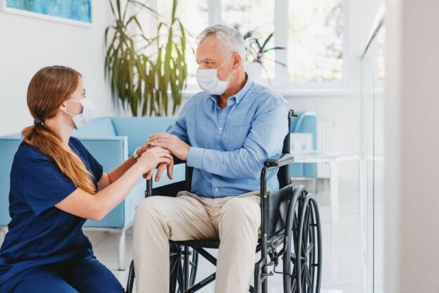 A nurse holding a hand of a man in a wheelchair