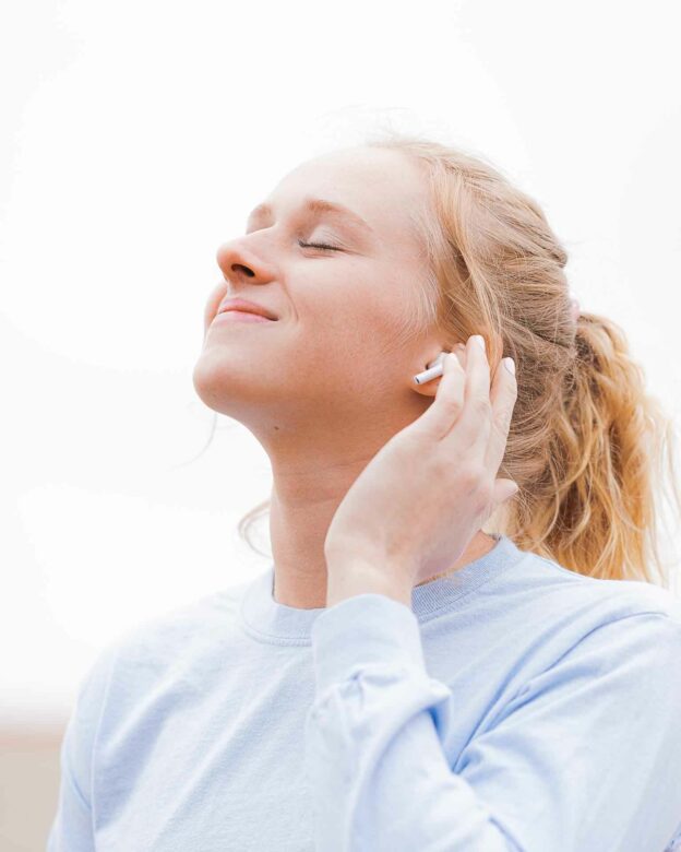 A person with her eyes closed holding a white earphone