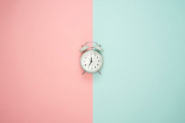 A white alarm clock on a pink and blue background