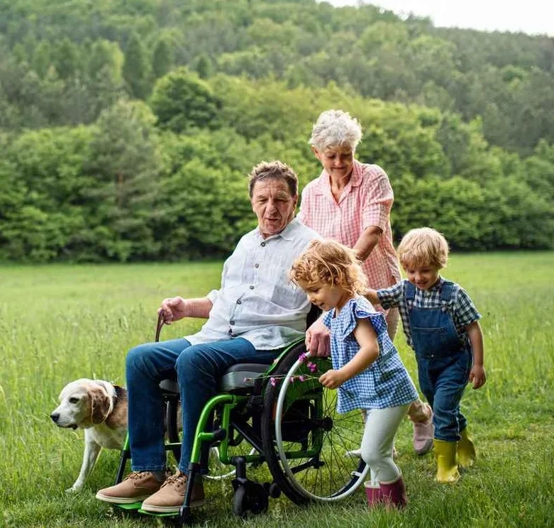 Family with man in wheelchair and dog walking in a field