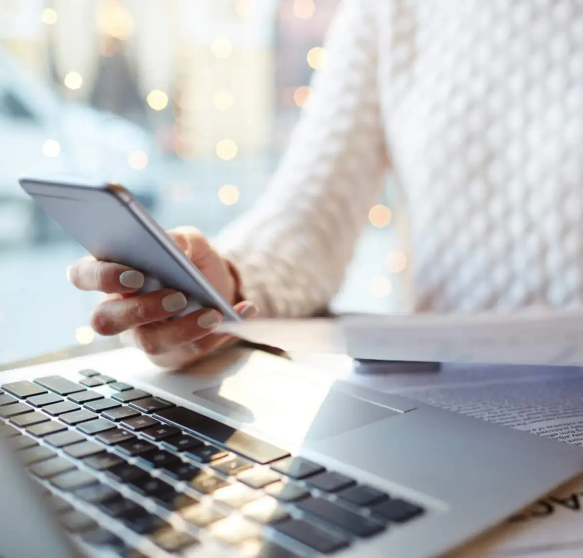 Women sitting at a laptop using mobile phone with papers in hand