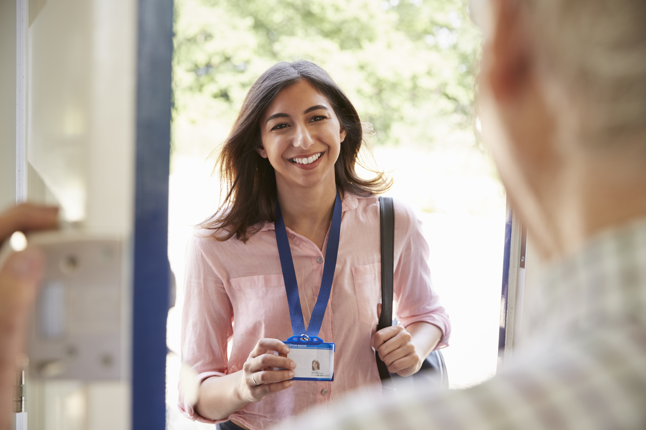Senior man opening front door to young woman showing ID card