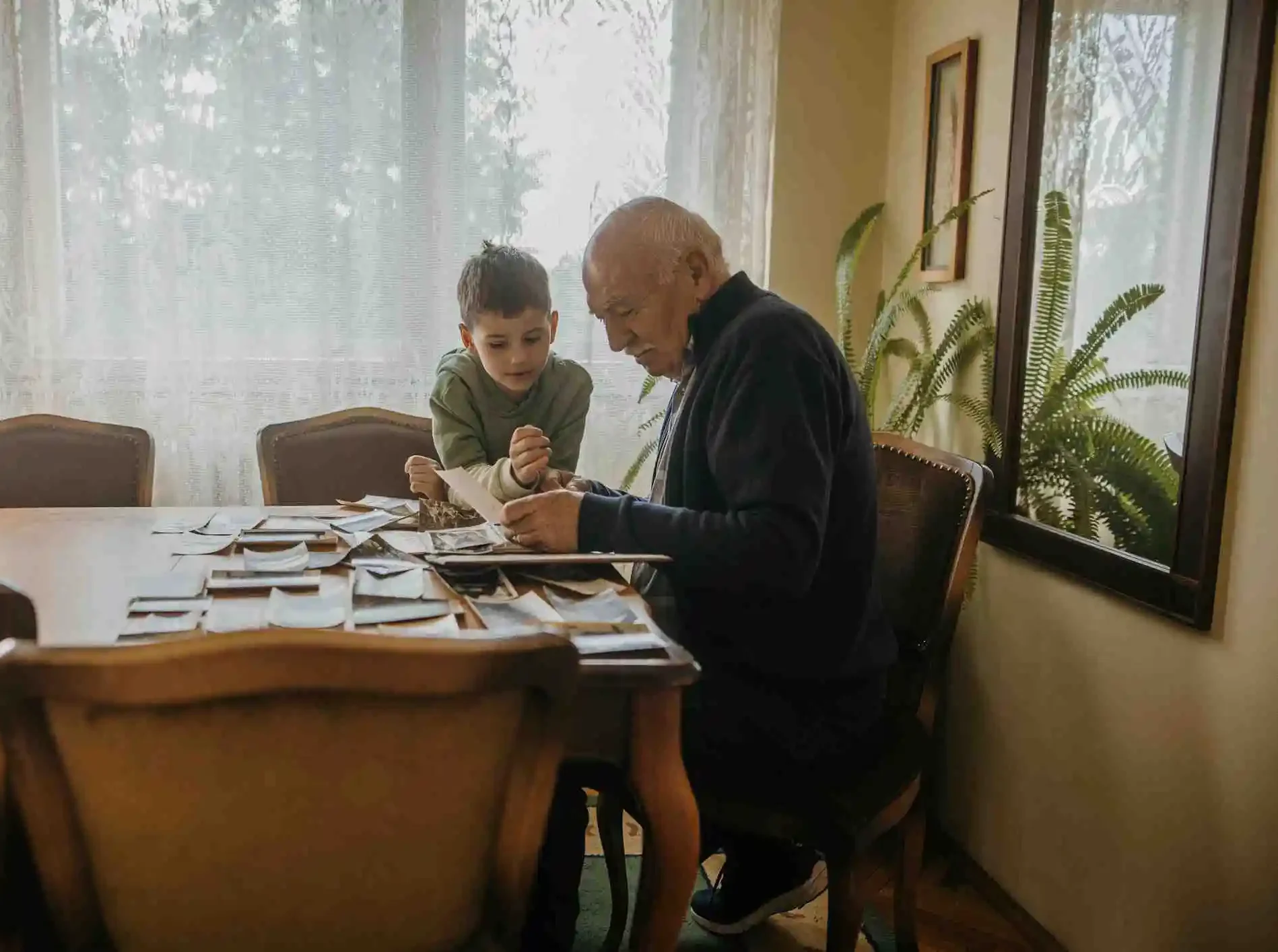 Elderly man with Alzheimer's with young grandson looking at photos at kichen table