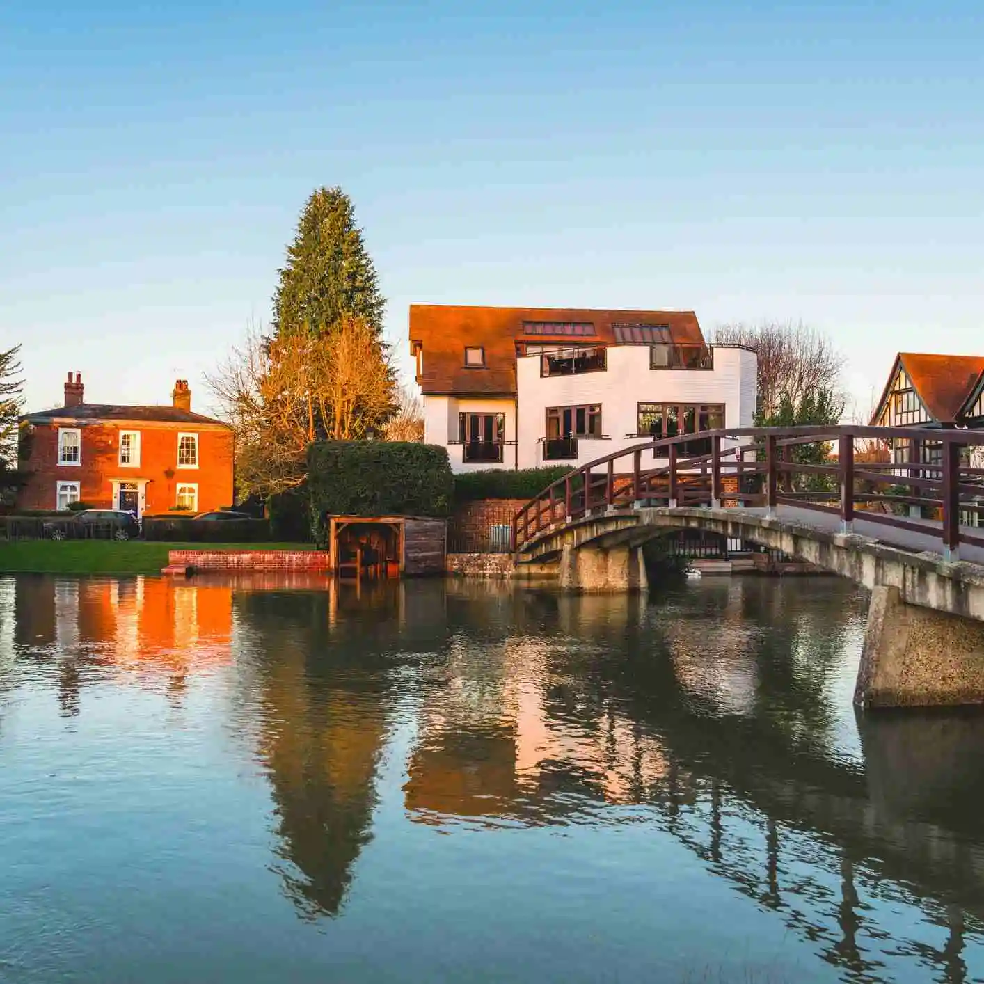 Houses on the banks of a river with bridge at sunset