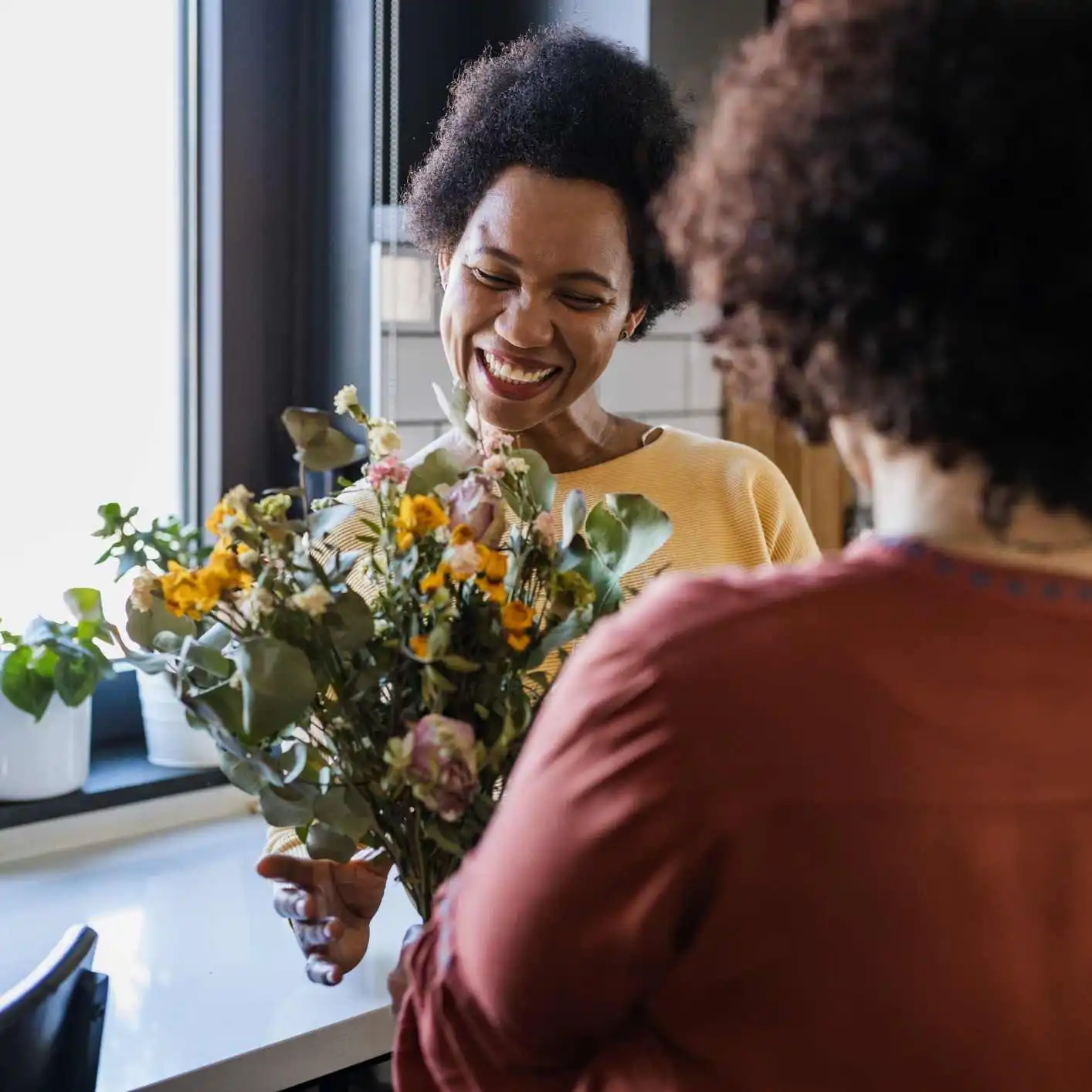 Smiling women holding flowers in a kitchen